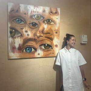 Lauren Doble, an young female artist, stood next to her artwork. Her hair is up and she is smiling.