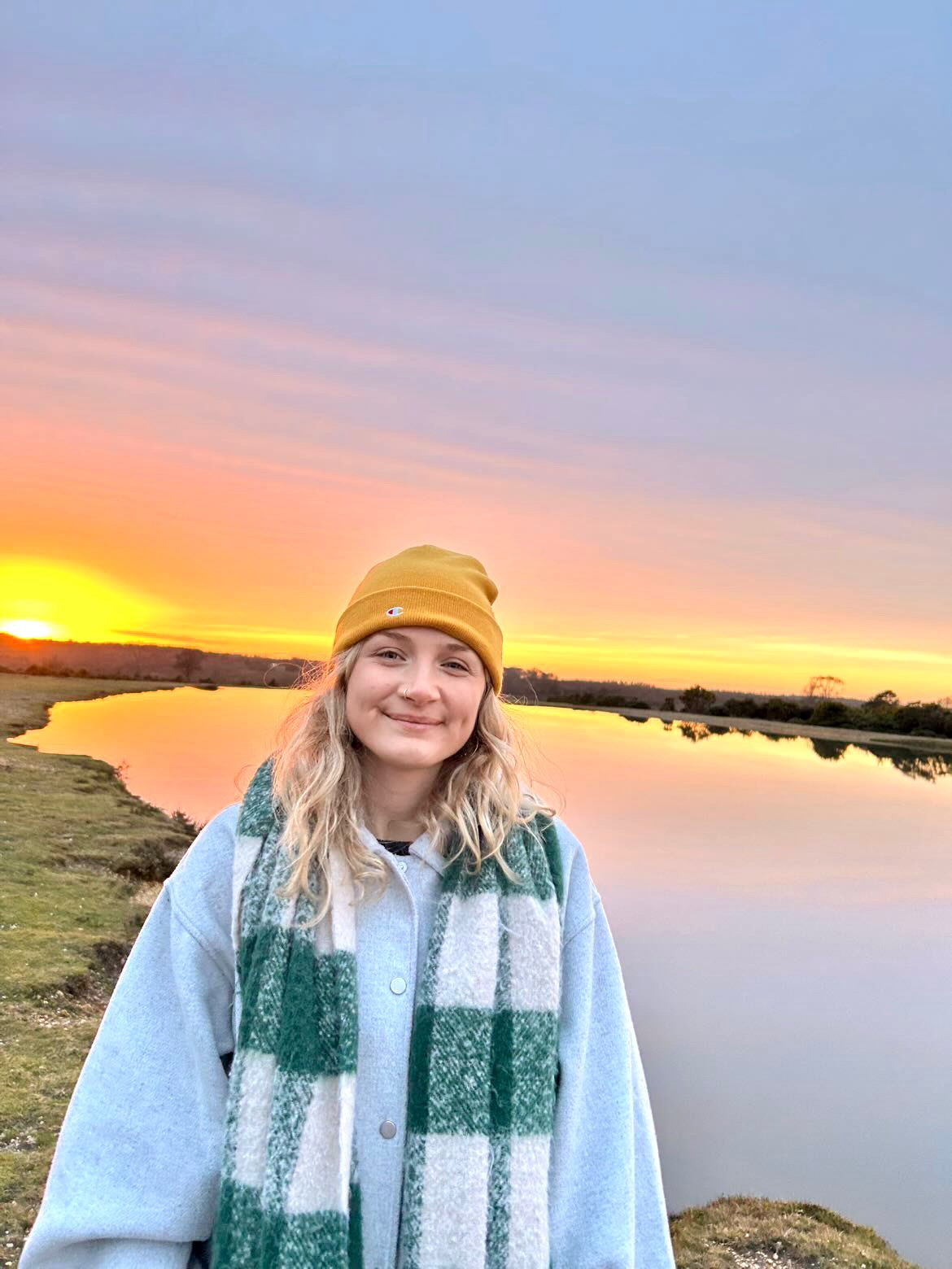 Lucy Tully, dorest based artist and illustrator outdoors at sunset next to a lake wearing winter clothing.