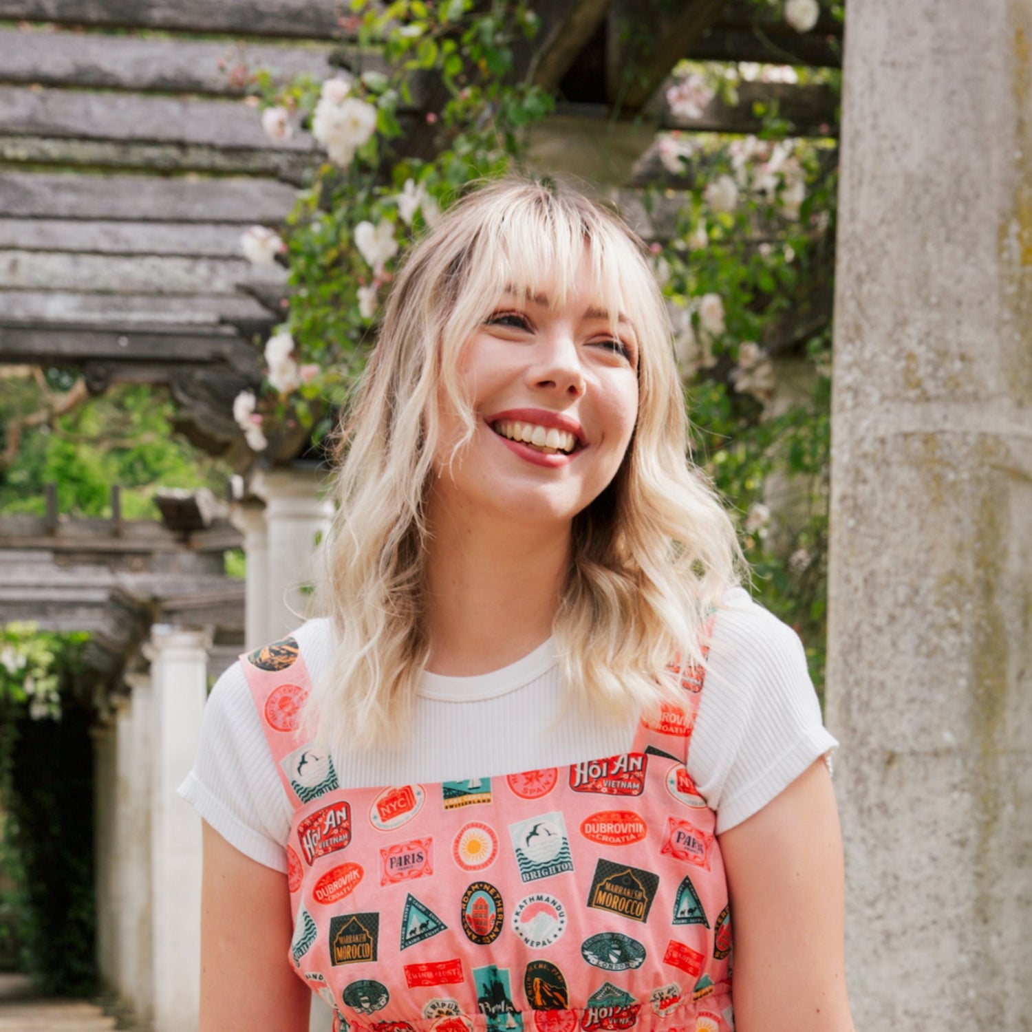 Artist Betty Woodhouse is smiling in the sunshine, wearing graphic pink dungarees.