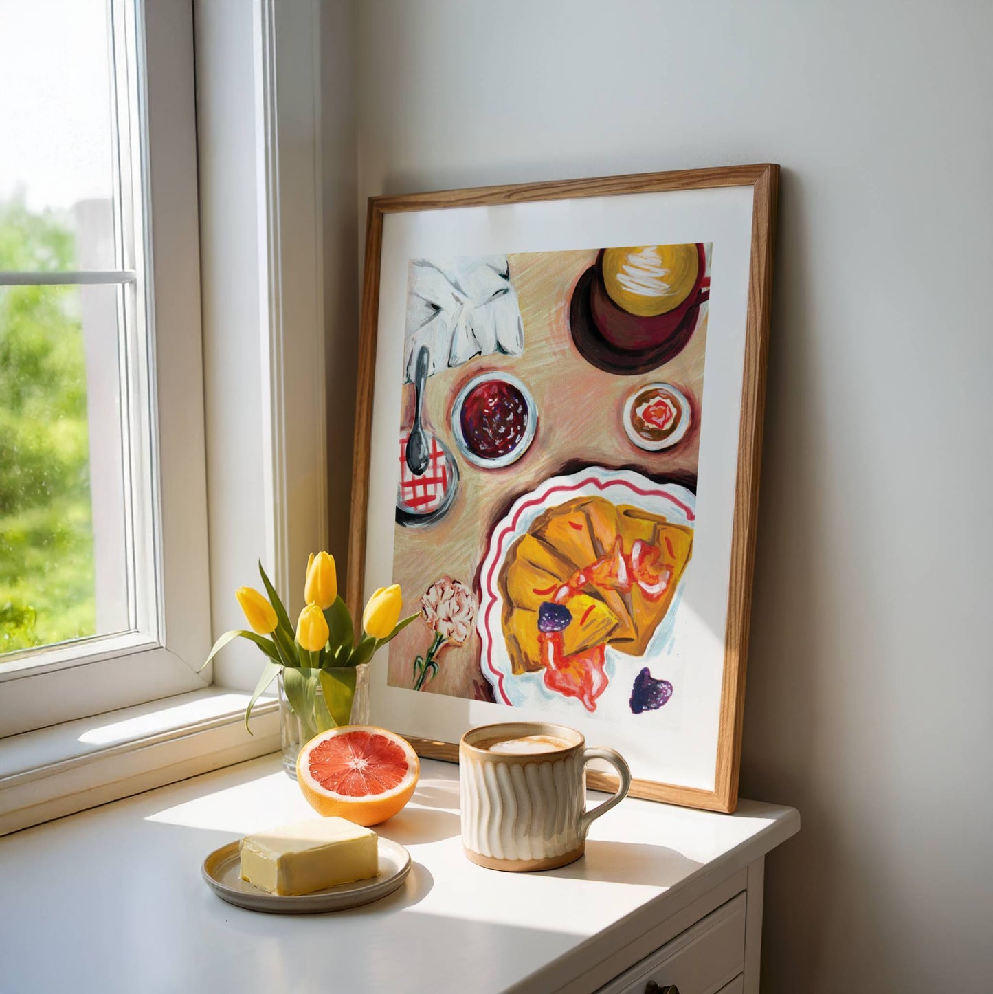 Framed artwork on a windowsill with a cup of coffee, grapefruit, and butter.